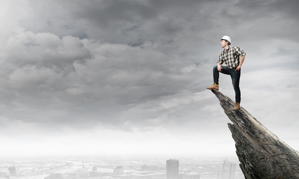 Successful project accounting client of Summit Business Advisors, an engineer perched at the top of a rock outcrop with urban skyline in background